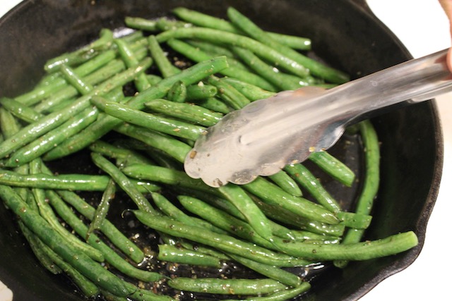 Green beans from a skillet being served with tongs